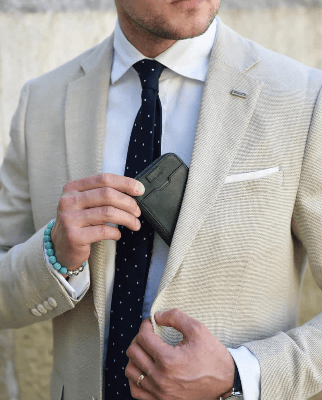 Man in a beige suit tucking the NOTTING HILL zip-around wallet into his jacket pocket