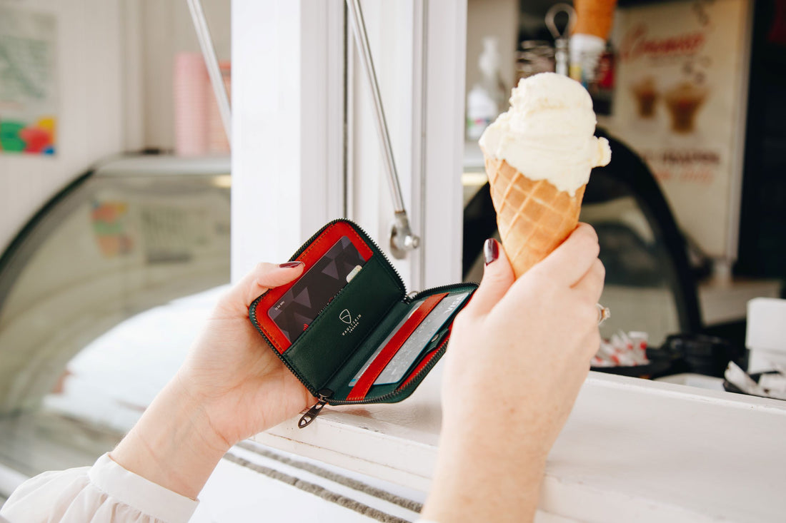 A hand opens a green NOTTING HILL wallet with cards while the other holds a vanilla ice cream cone