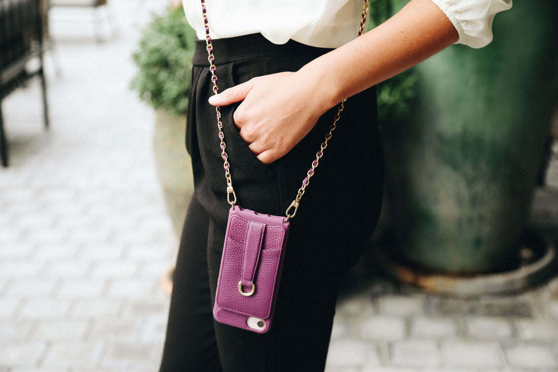 A woman wears a purple leather phone pouch on a gold chain crossbody strap