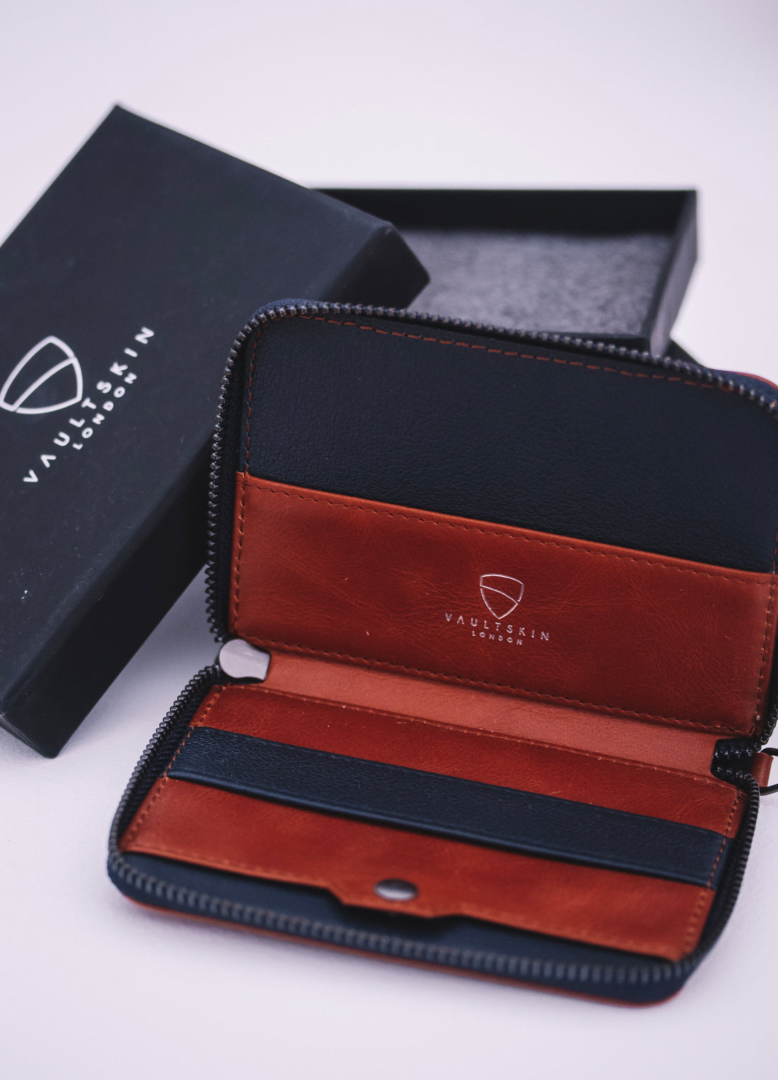 Open NOTTING HILL zip-around wallet in navy and brown leather beside its black branded gift box