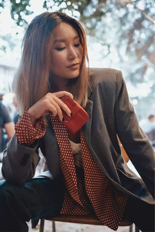 Woman sitting on a chair looking on the floor, holding a red zipper wallet into the centre of the picture
