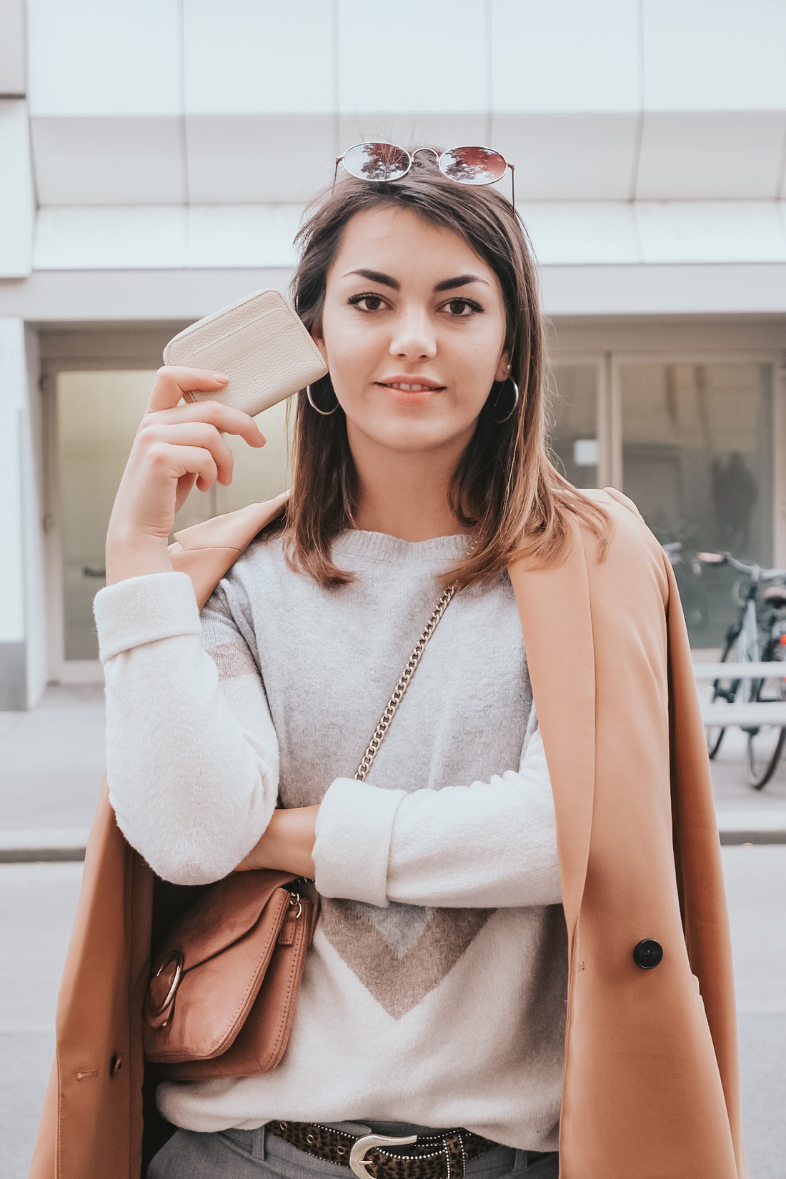 Woman wearing sunglasses holds a BELGRAVIA zipper wallet out on a street