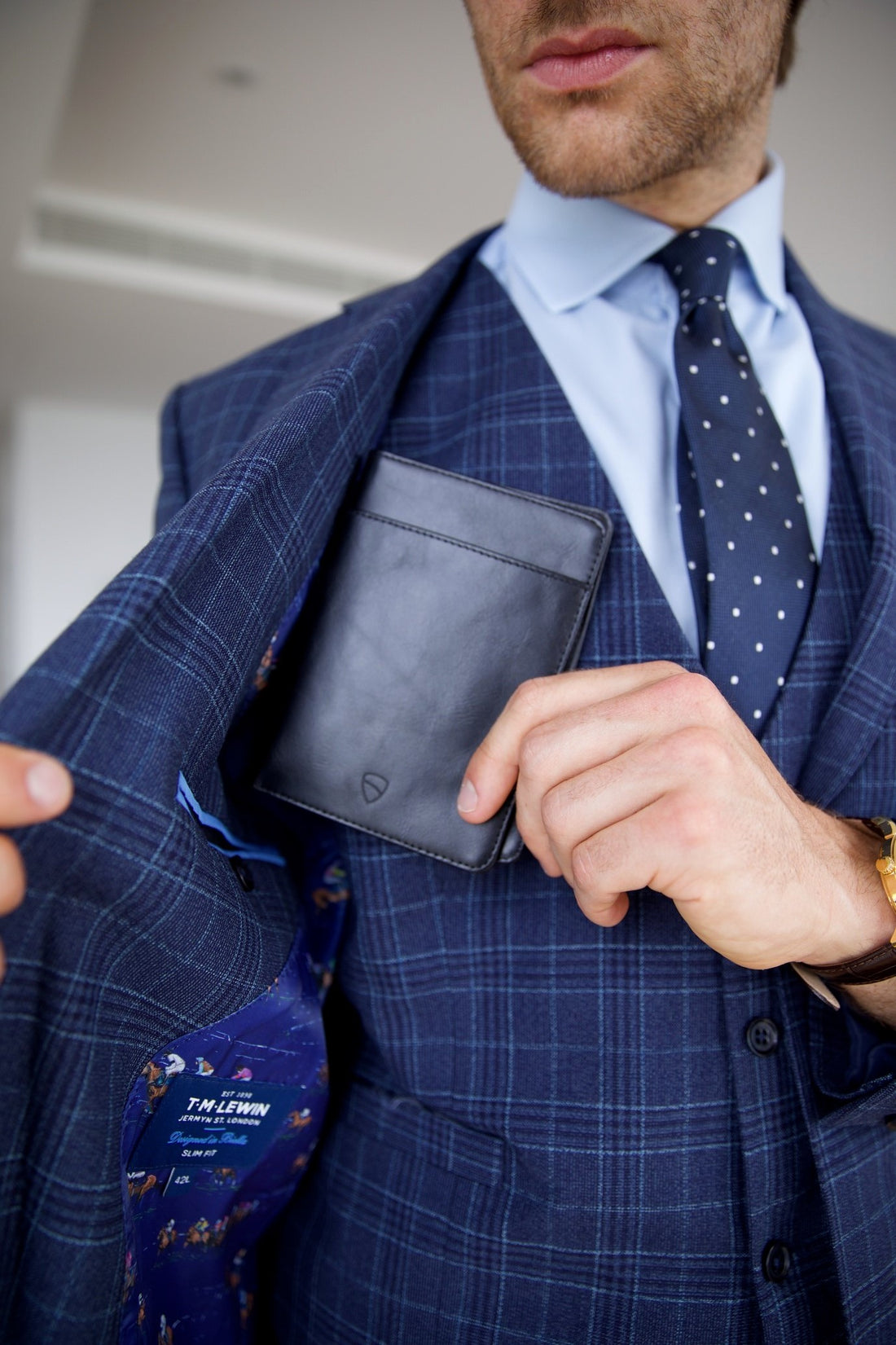 A man in a navy plaid suit pulls a black leather card holder from his breast pocket