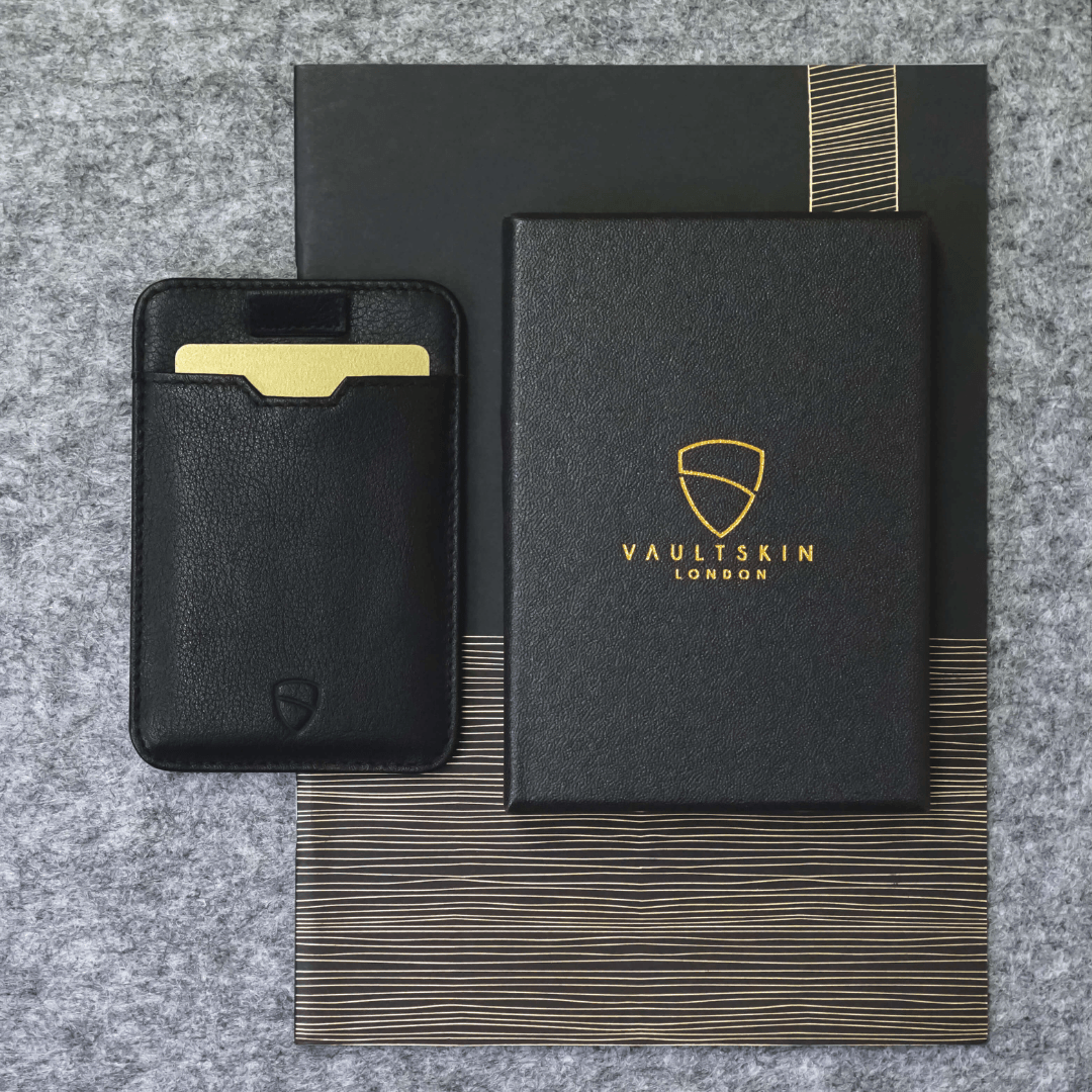 Black leather card holder with a gold card inside, beside a branded gift box on dark packaging