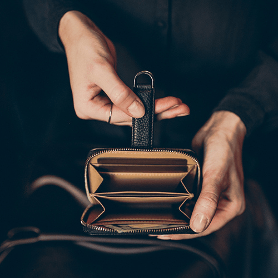 Hands open a black leather zip-around wallet with a key ring, showing empty card slots inside