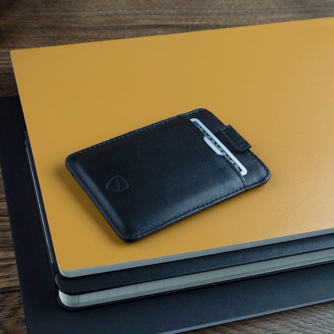 A black leather card holder with a pull tab holds 1 card, resting on a yellow notebook