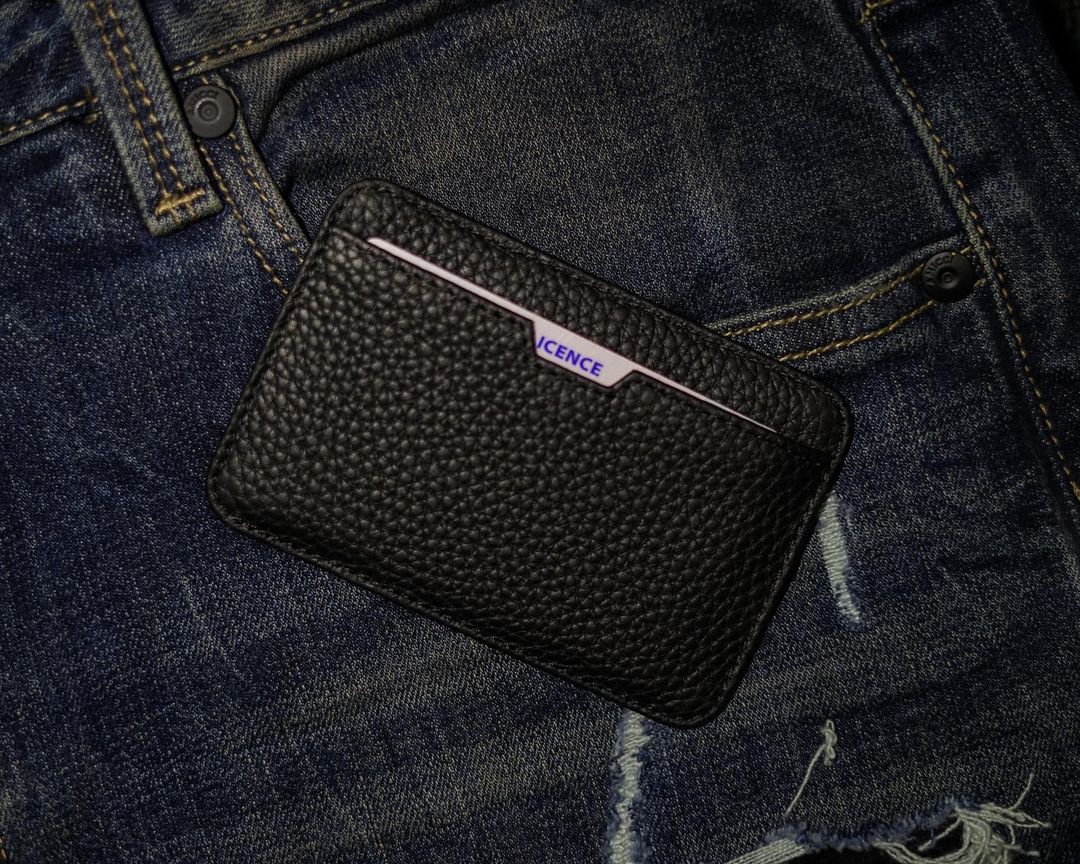 A matt black CHELSEA card holder resting on denim jeans with a card peeking out