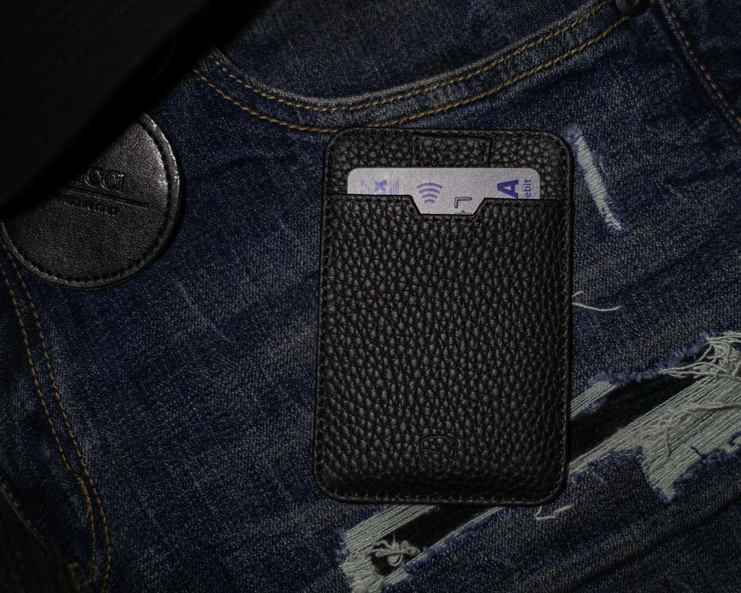 A black leather card holder with a bank card tucked inside sits on denim fabric