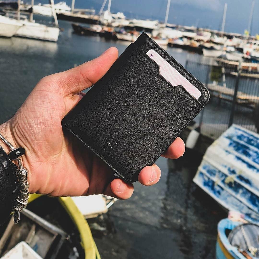 A hand holds a black leather card holder with a card peeking out above a marina full of boats