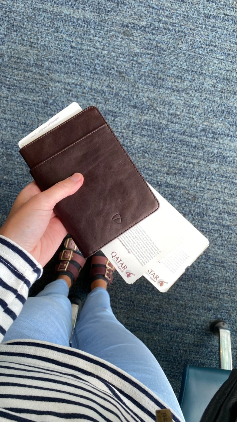 Hand holding a brown leather passport holder with boarding passes tucked inside above a denim lap