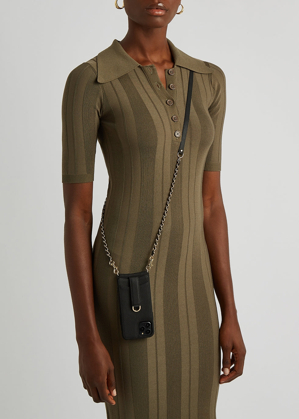 Woman in an olive dress wears a black leather phone pouch on a gold chain crossbody strap