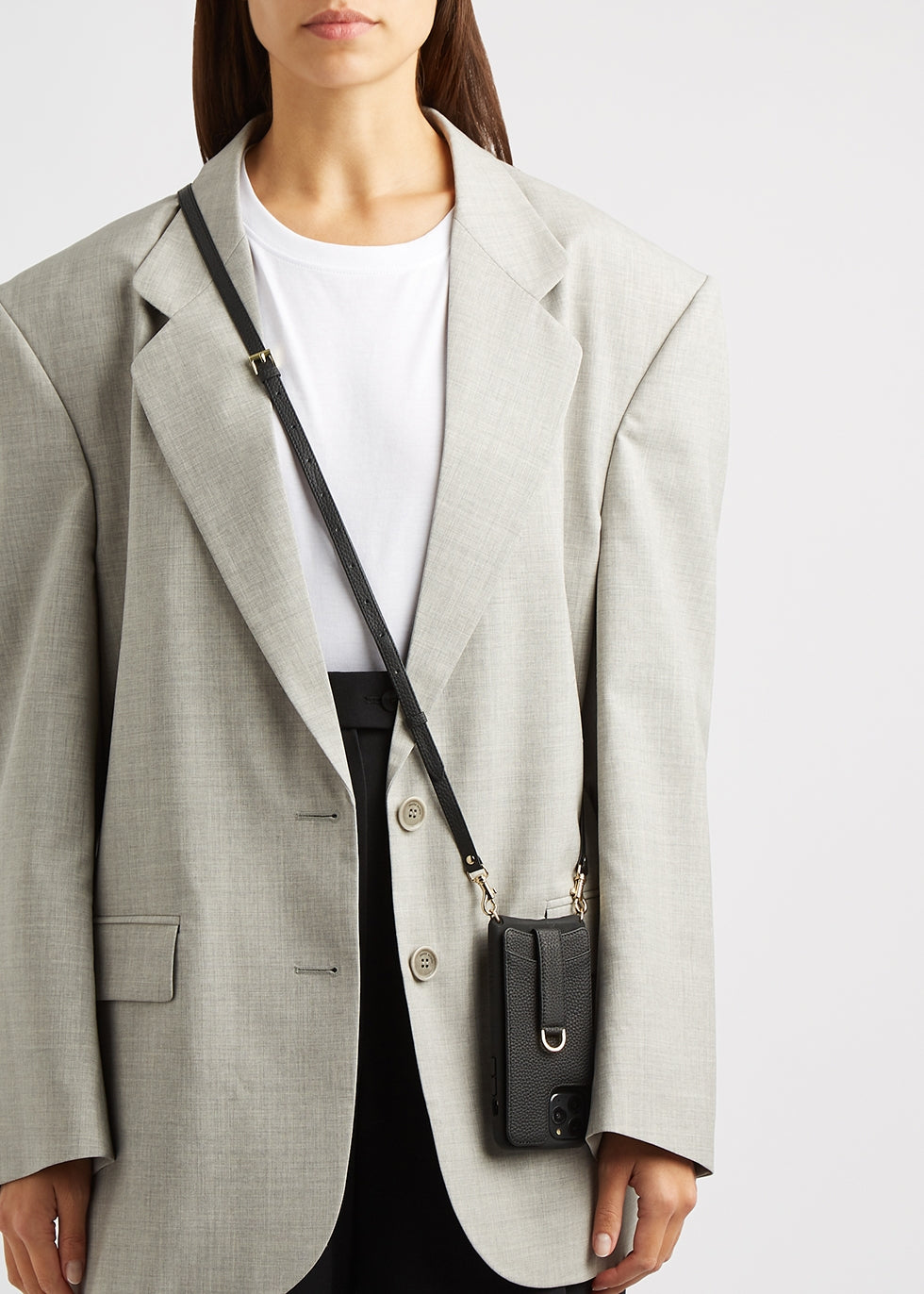 Woman in a grey blazer wearing a black leather phone case on a crossbody strap