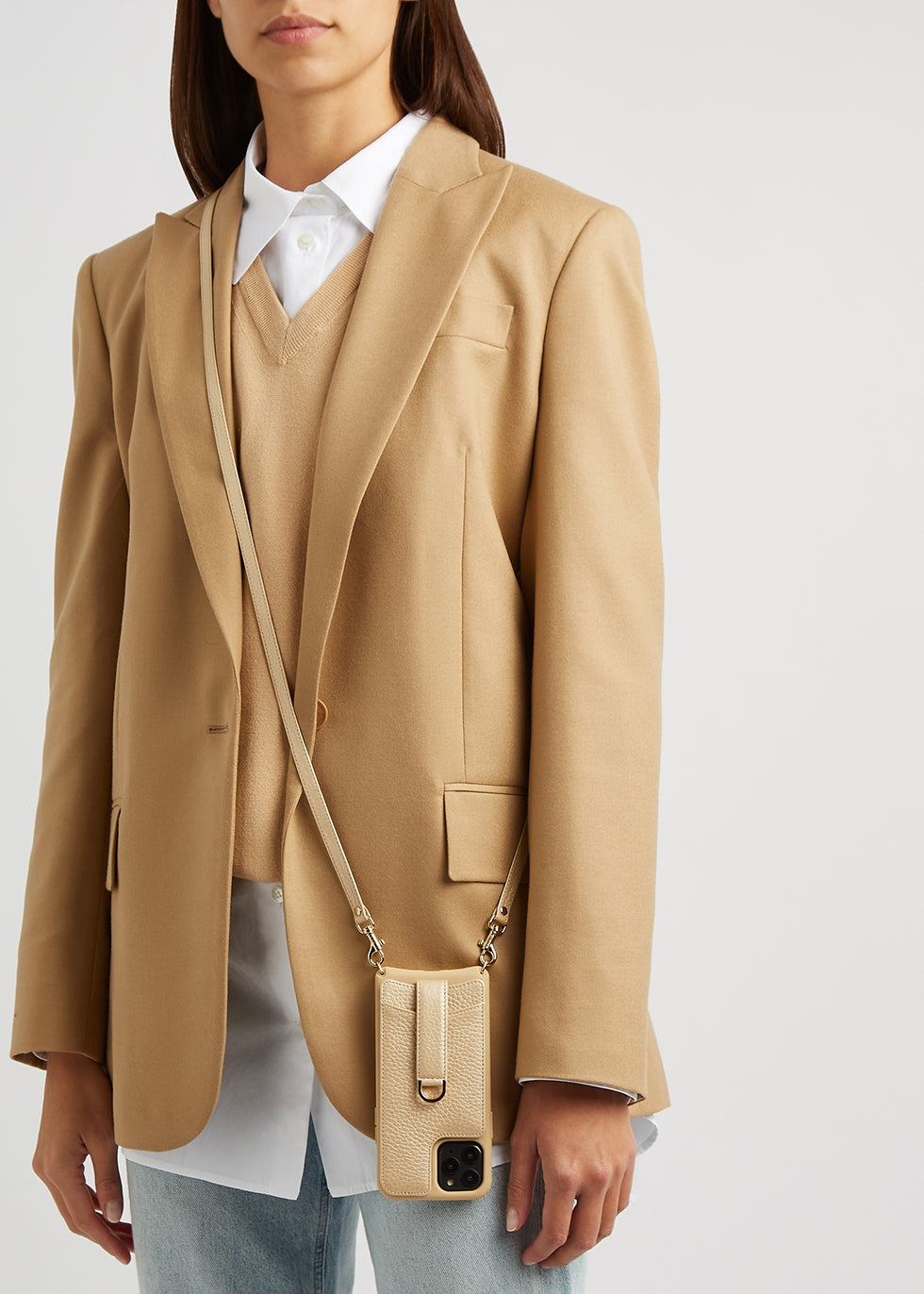 Woman in a tan blazer carries an ivory leather phone case with a card slot on a crossbody strap
