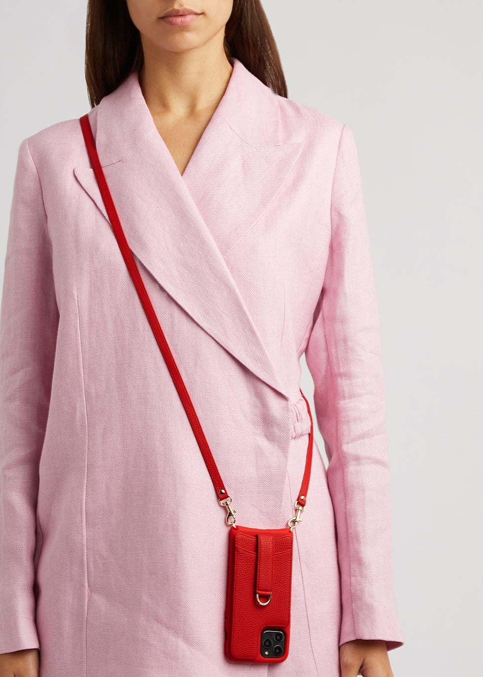Woman in a pink blazer carries a red leather VICTORIA phone case on a crossbody strap