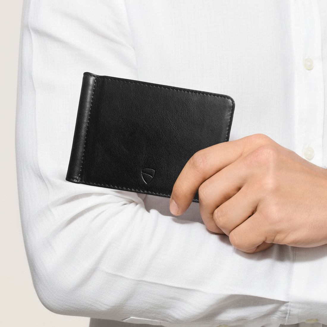 A hand holds a BROMPTON black leather money-clip wallet against a shirt sleeve
