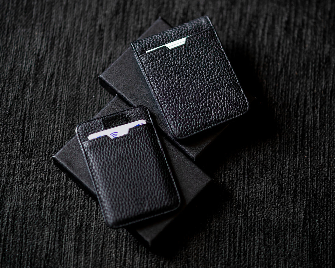 Two black leather card holders with cards tucked inside resting on black boxes on a dark surface