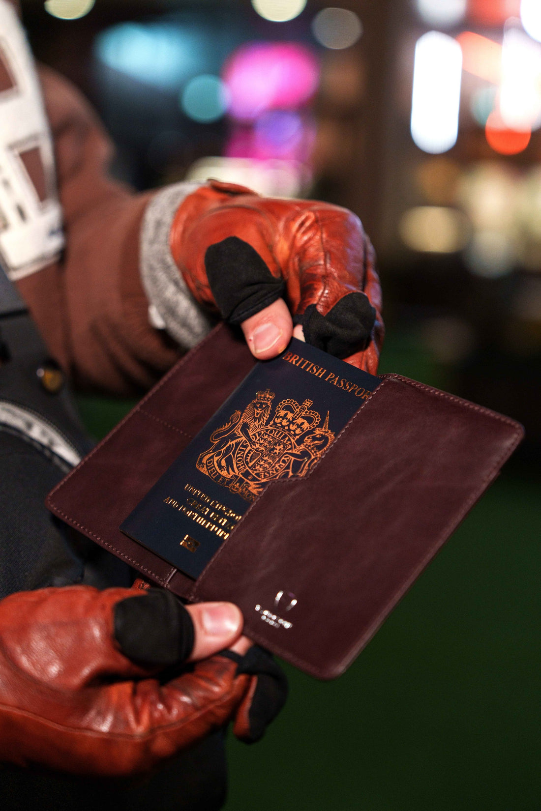 A gloved hand holds a KENSINGTON passport holder with a passport tucked inside at night