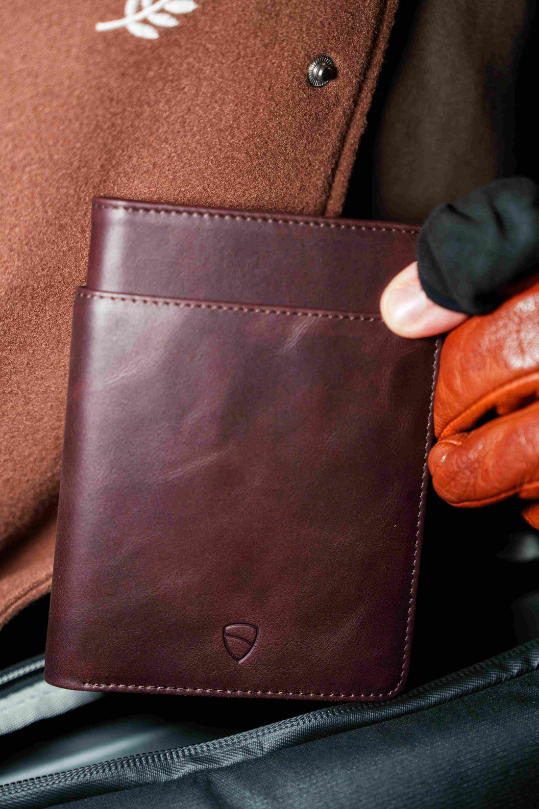 A gloved hand pulls a burgundy KENSINGTON passport wallet from a coat pocket