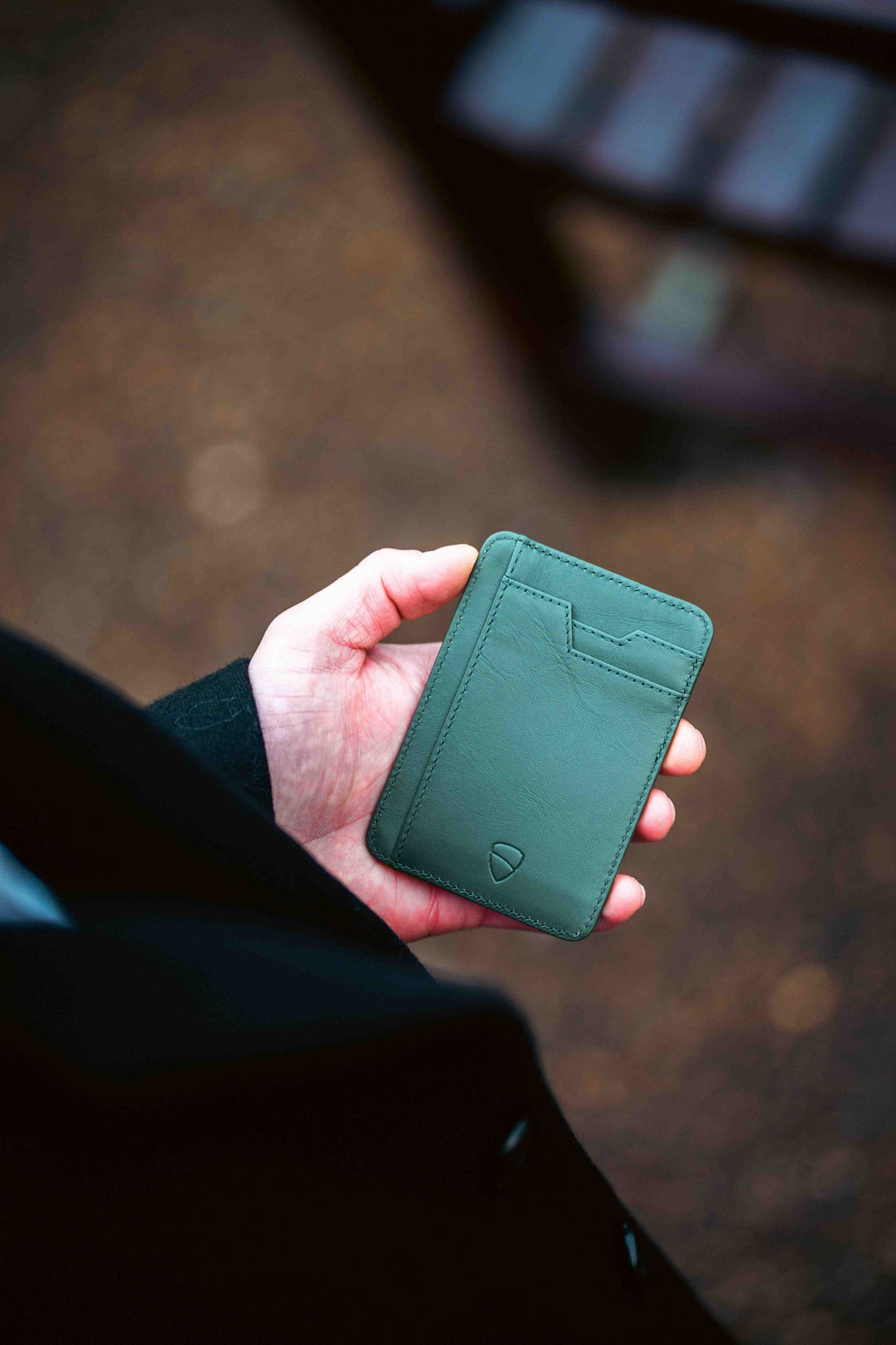 A hand holds a green leather BRIXTON card holder with visible stitching and stacked card slots