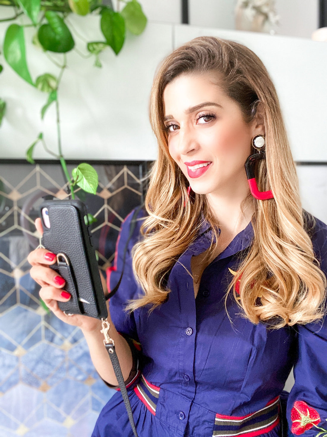 Woman with long wavy hair holds a black leather phone case with a wrist strap