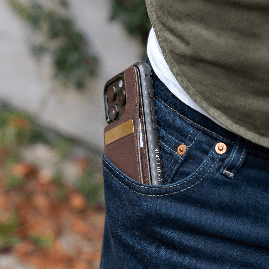 A brown leather card holder with 2 cards attached to a phone in a denim pocket