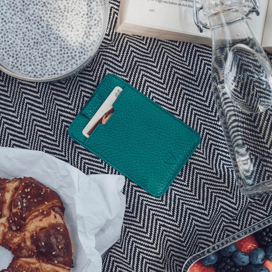 Teal CHELSEA card holder with a card peeking out, surrounded by breakfast items on a herringbone cloth