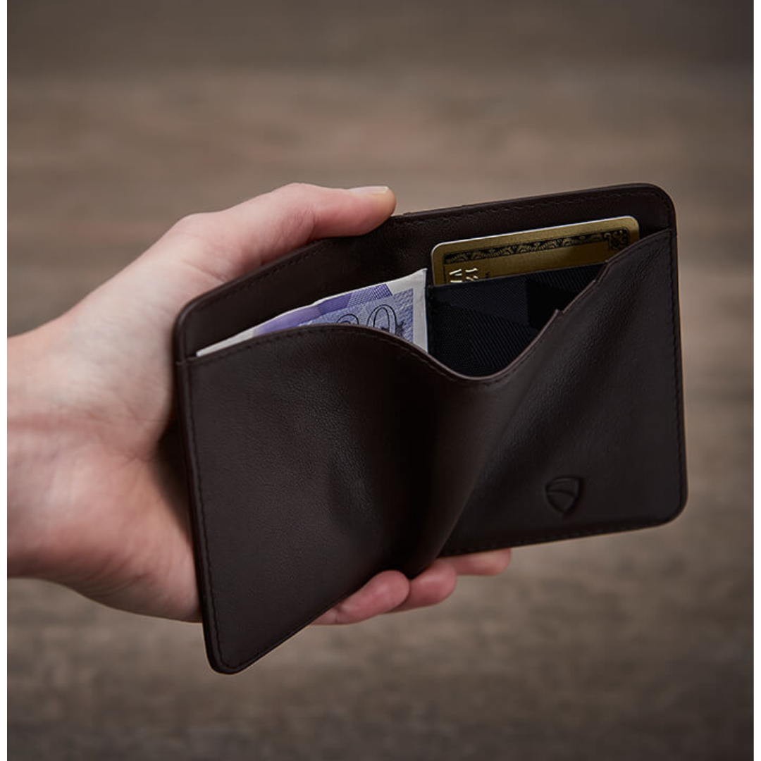 A hand holds an open brown leather CITY wallet with a folded banknote and 2 cards tucked inside
