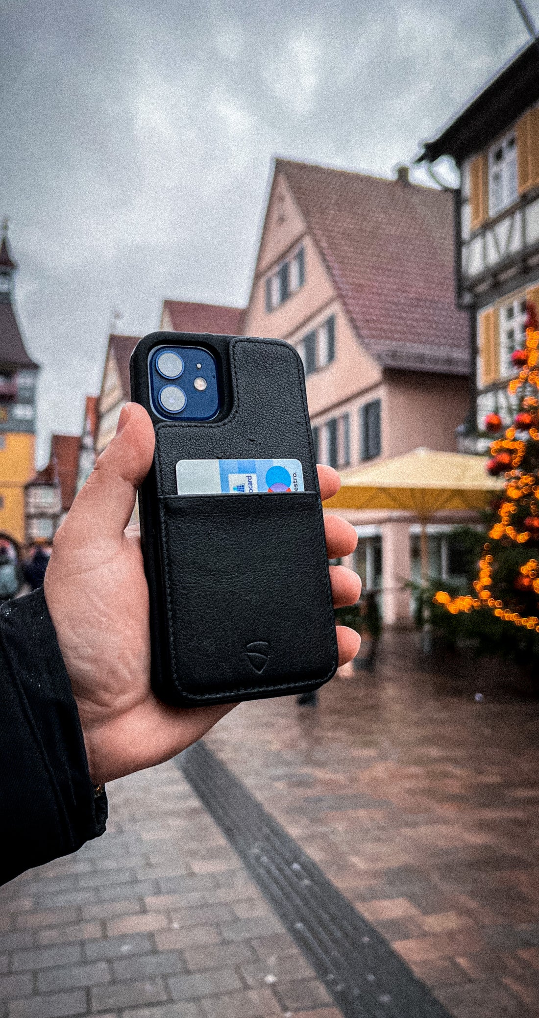 A hand holds a black ETON ARMOUR phone case with a card tucked in its back pocket outdoors