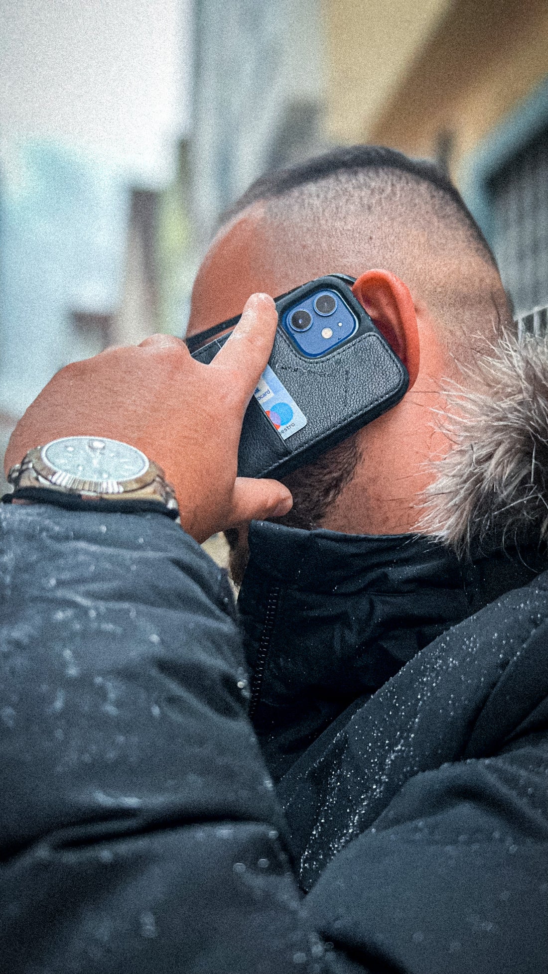 A man holds a smartphone to his ear with a card tucked into a black leather case on the back