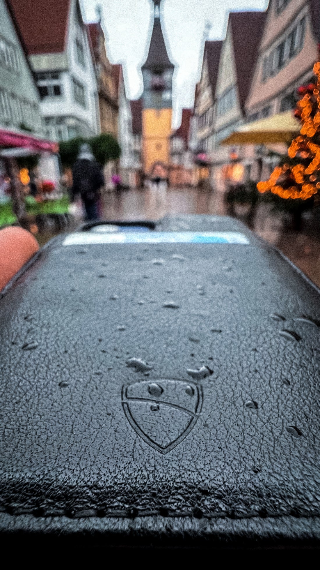 Raindrops cover a leather wallet embossed with a shield logo on a rainy European street