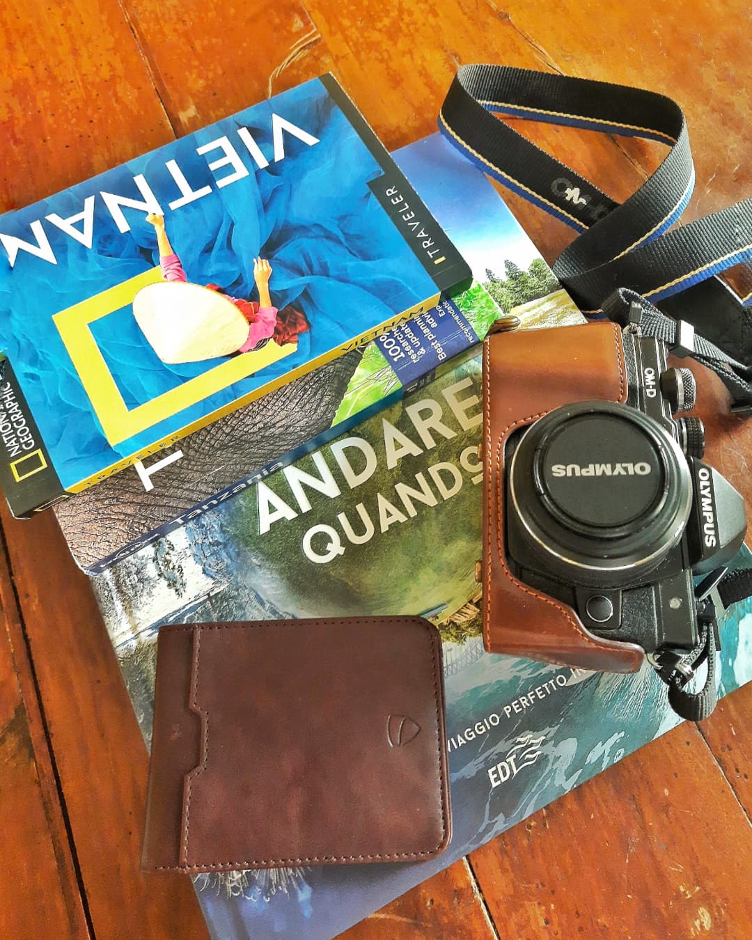 A MANHATTAN wallet rests beside a camera in a leather case, a strap, and two travel guidebooks