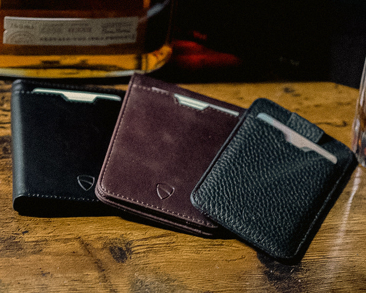 Three leather card holders in black, burgundy and black stand fanned out on a wooden table