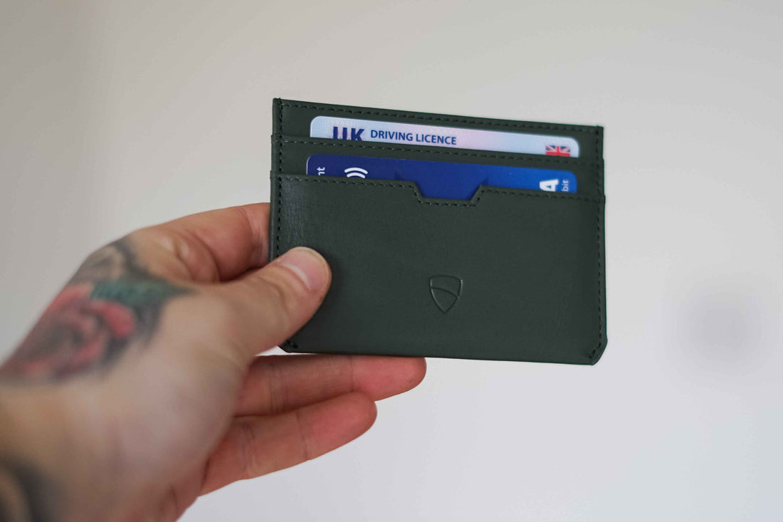 A hand holds a green MOORGATE cardholder with a driving licence and bank card tucked inside