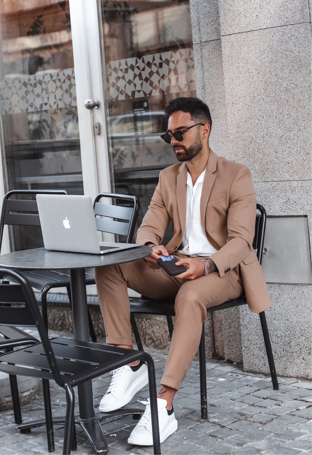 Men sits with NOTTING HILL wallet in a cafe with laptop in front