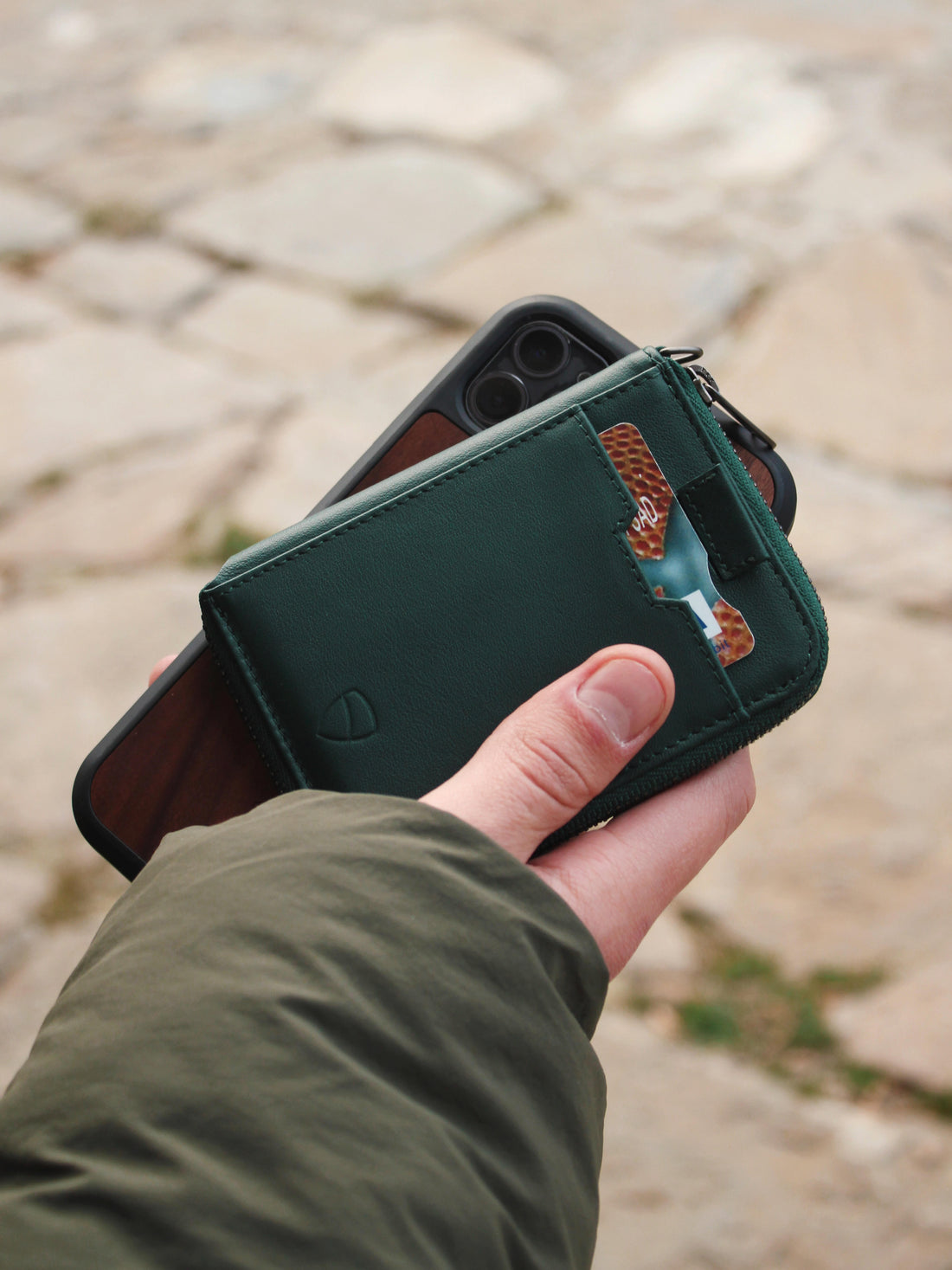 A hand holds a green NOTTING HILL zip-around wallet with a card tucked in its strap over a phone