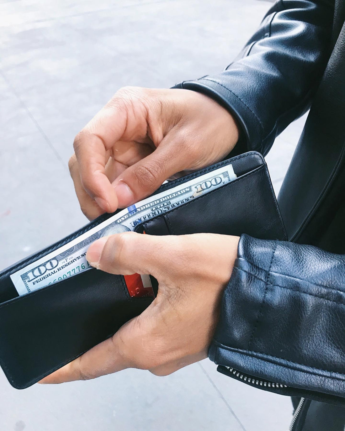 Hands remove a flat unfolded $100 bill from a black leather MANHATTAN bifold wallet