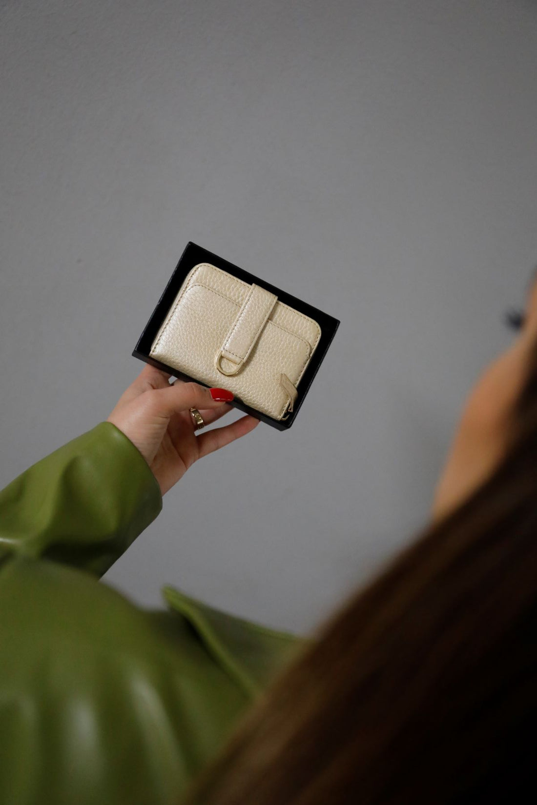 Woman with red nail polish holds a cream leather wallet with a tab closure in a black gift box