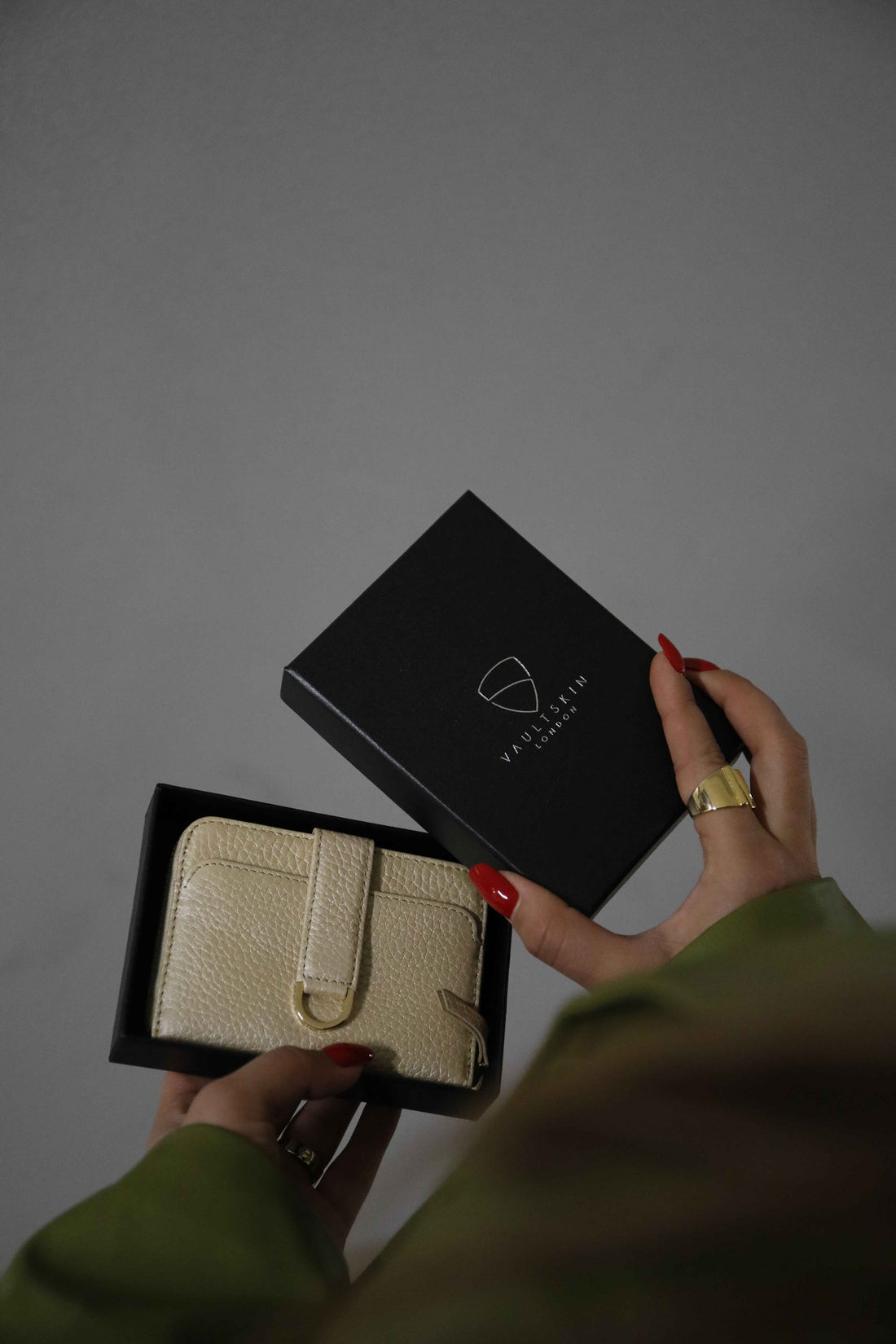 Hands with red nail polish hold a cream leather wallet beside its black branded gift box
