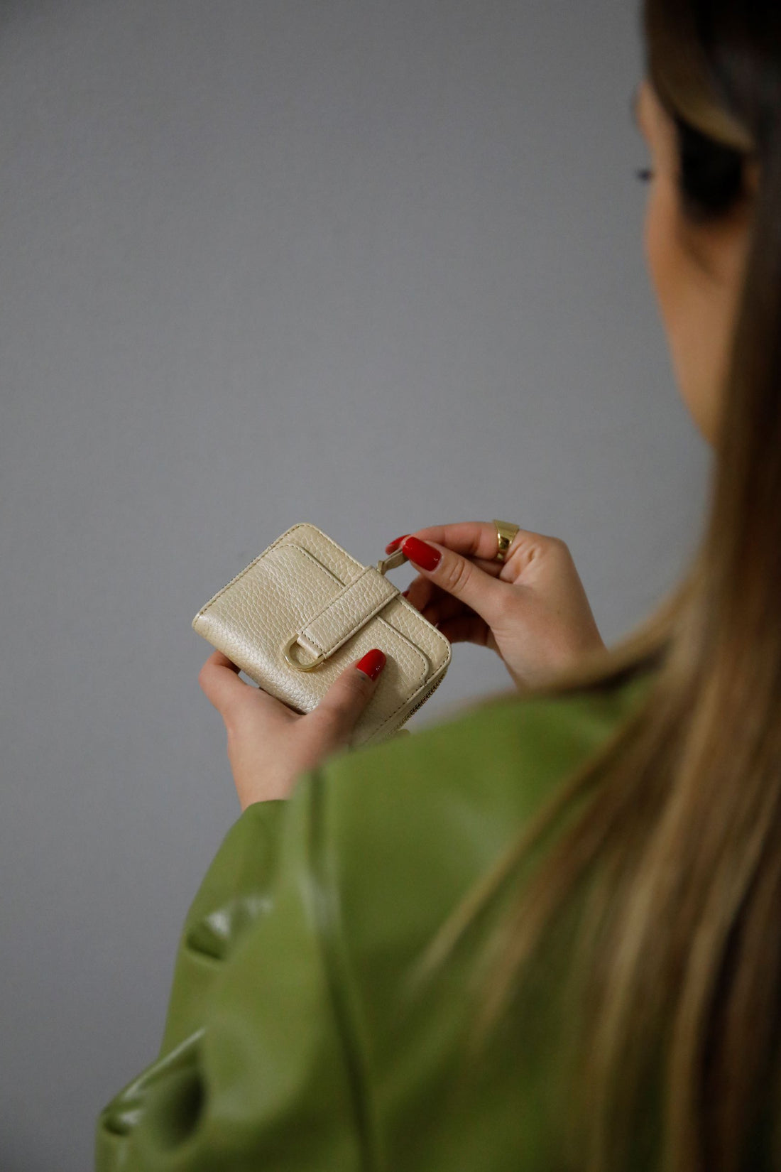 A woman with red nail polish opens a cream leather zip wallet while wearing a green jacket