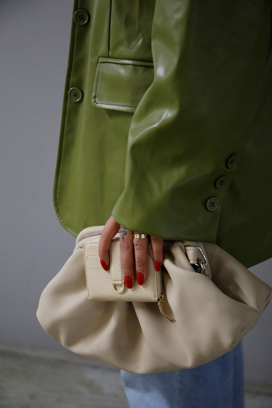 Hand with red nails holds a cream textured wallet while carrying a slouchy beige bag