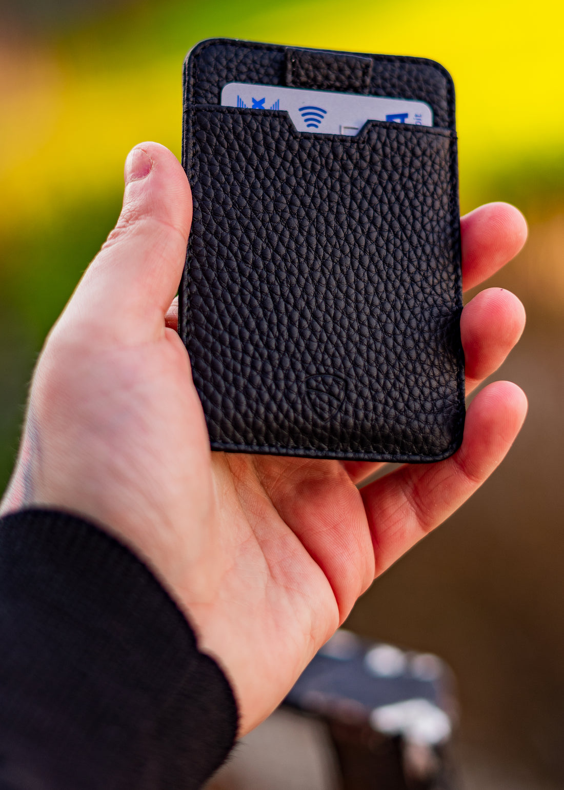 A hand holds a black leather card holder with several cards tucked inside, including one with a contactless symbol