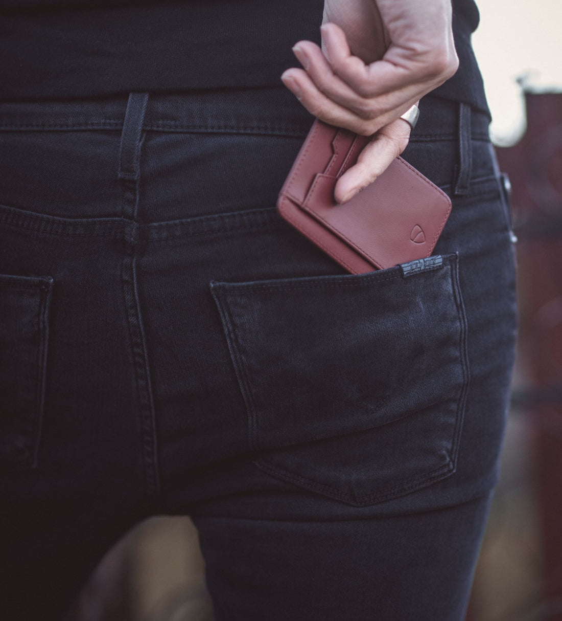 A hand pulls a brown Vaultskin BRIXTON card holder from the back pocket of black jeans