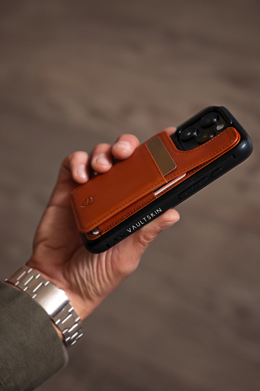 A hand holds a smartphone fitted with a cognac leather ETON wallet case holding a card