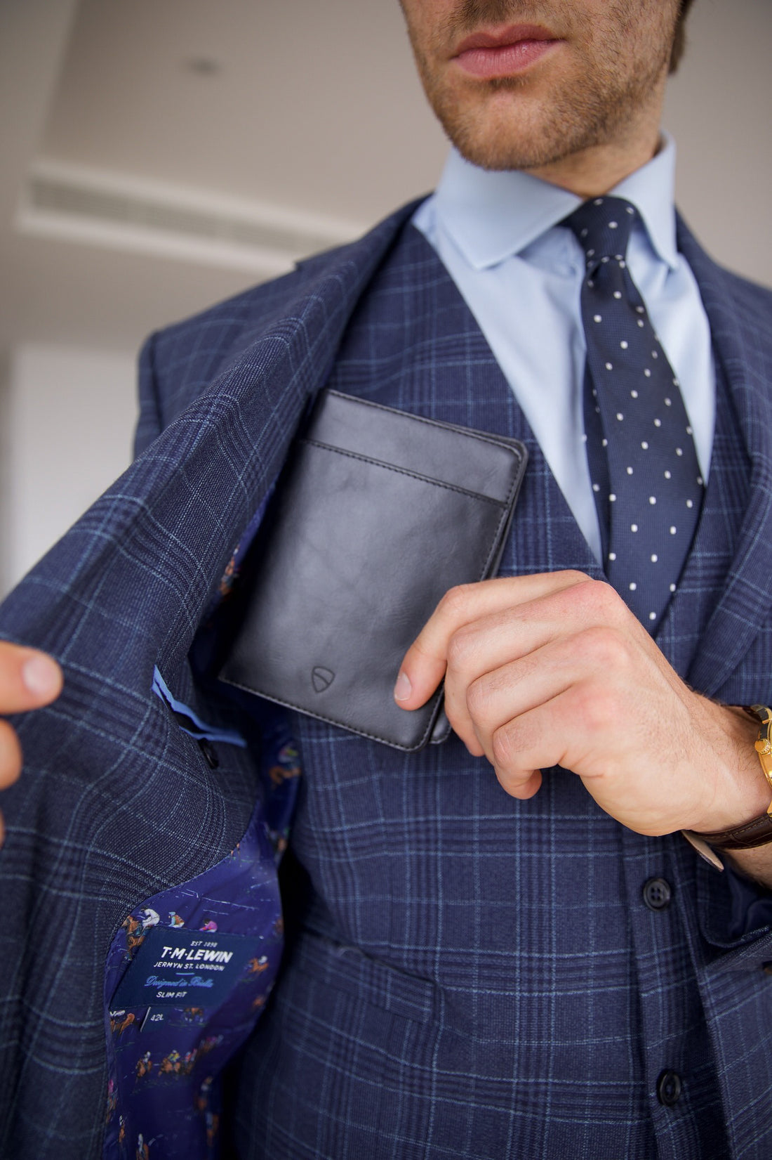 Man in a blue plaid suit tucks a black KENSINGTON passport holder into his jacket pocket