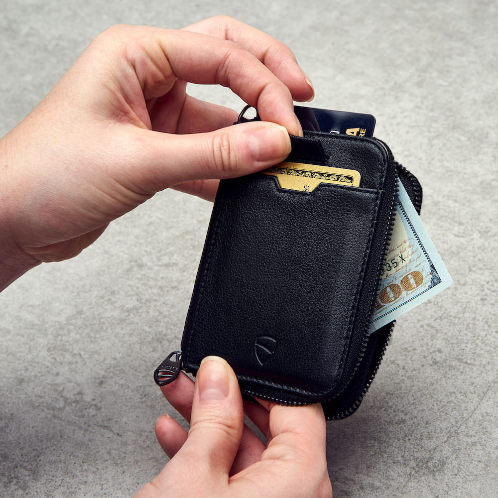 Hands unzip a NOTTING HILL leather wallet revealing 2 cards and folded cash inside