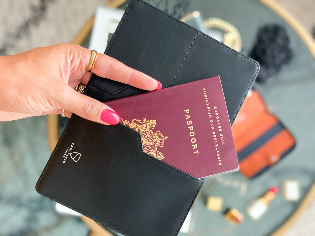 A hand with pink nail polish holds a KENSINGTON passport holder containing a maroon European passport