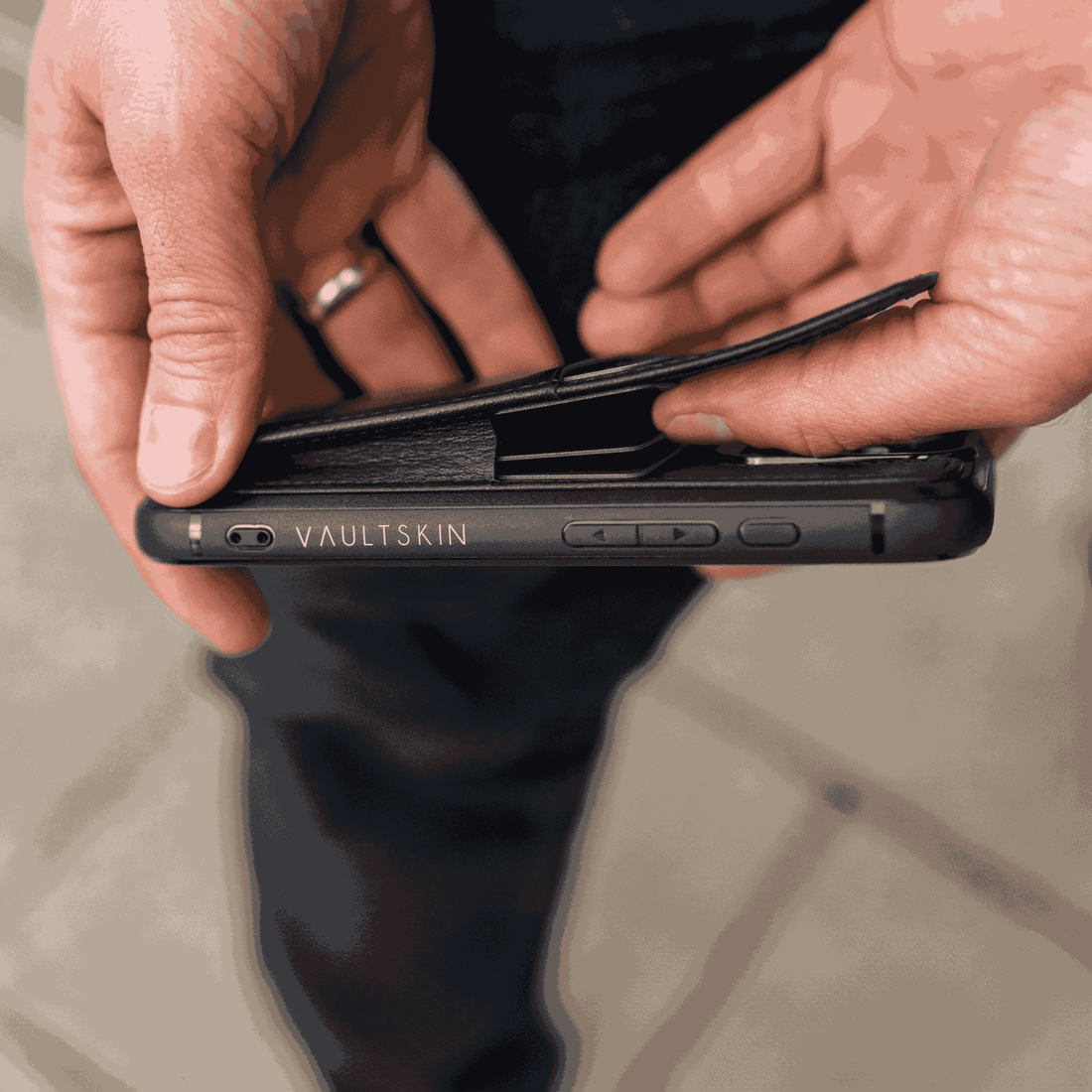 Two hands open a black leather iPhone case to reveal a card slot built into the back cover