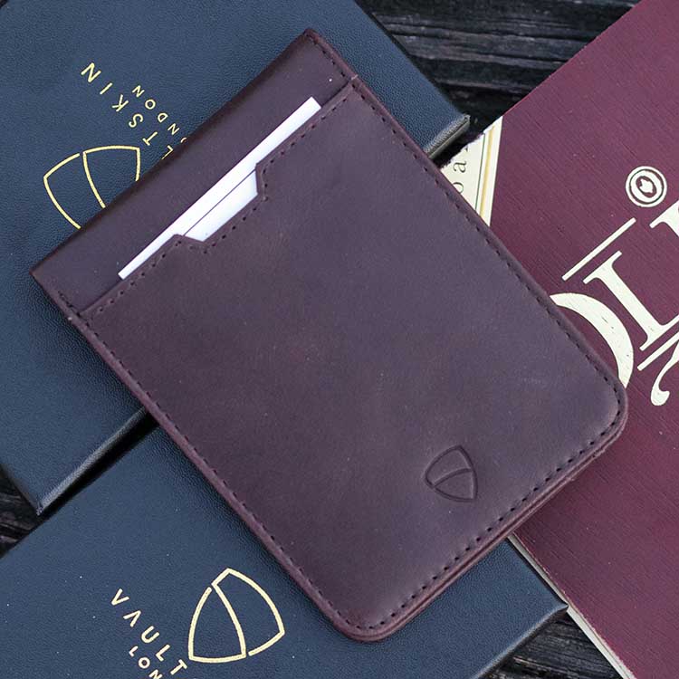 MANHATTAN brown leather bifold wallet with white cards tucked in its front pocket, resting on branded boxes
