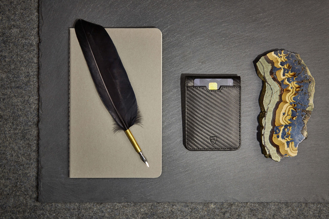 A quill pen rests on a notebook beside a black leather card holder and a polished stone slice