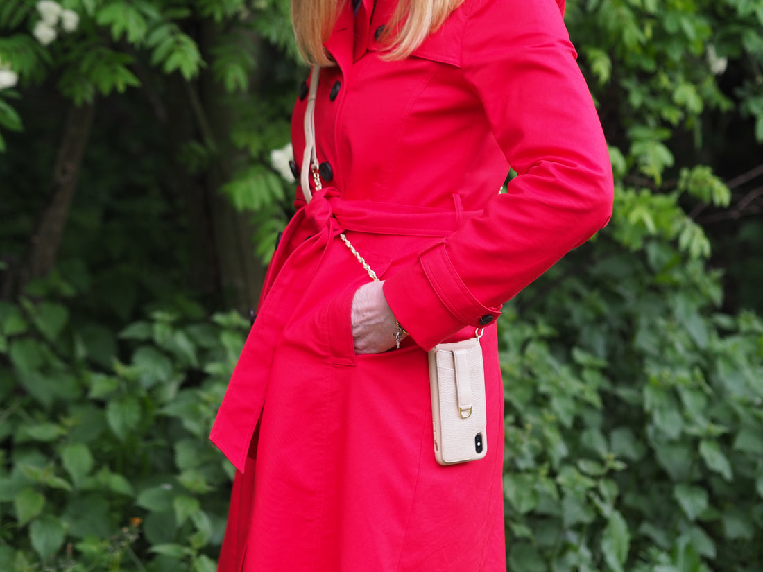 Woman in a red coat holding a cream leather phone case attached to a gold chain strap